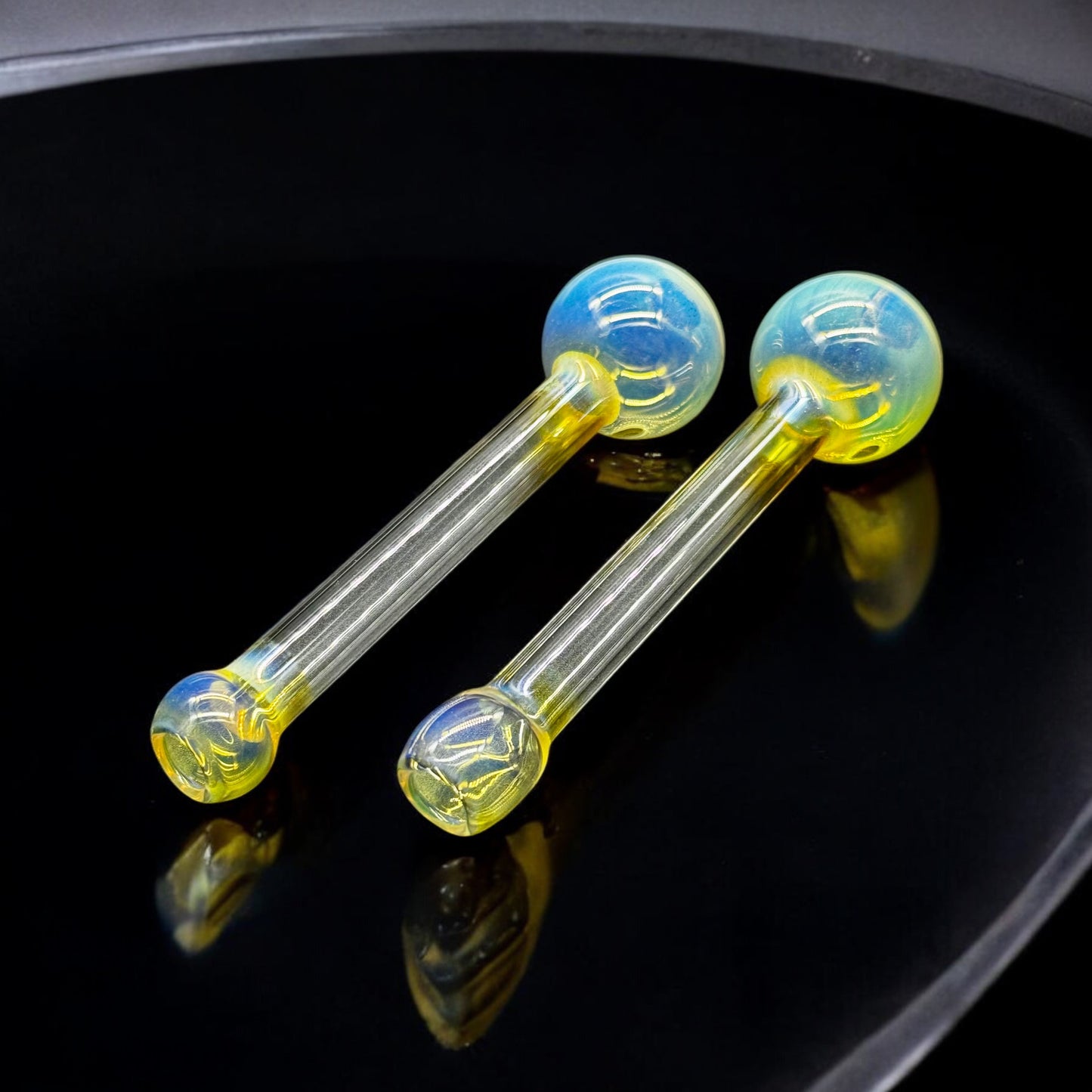 Pair of 5-inch hand-blown Pyrex oil burner pipes with fumed yellow-blue color under soft light