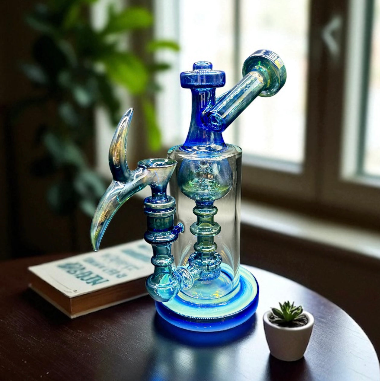 Blue glass water pipe on a table with a book and small plant in the background