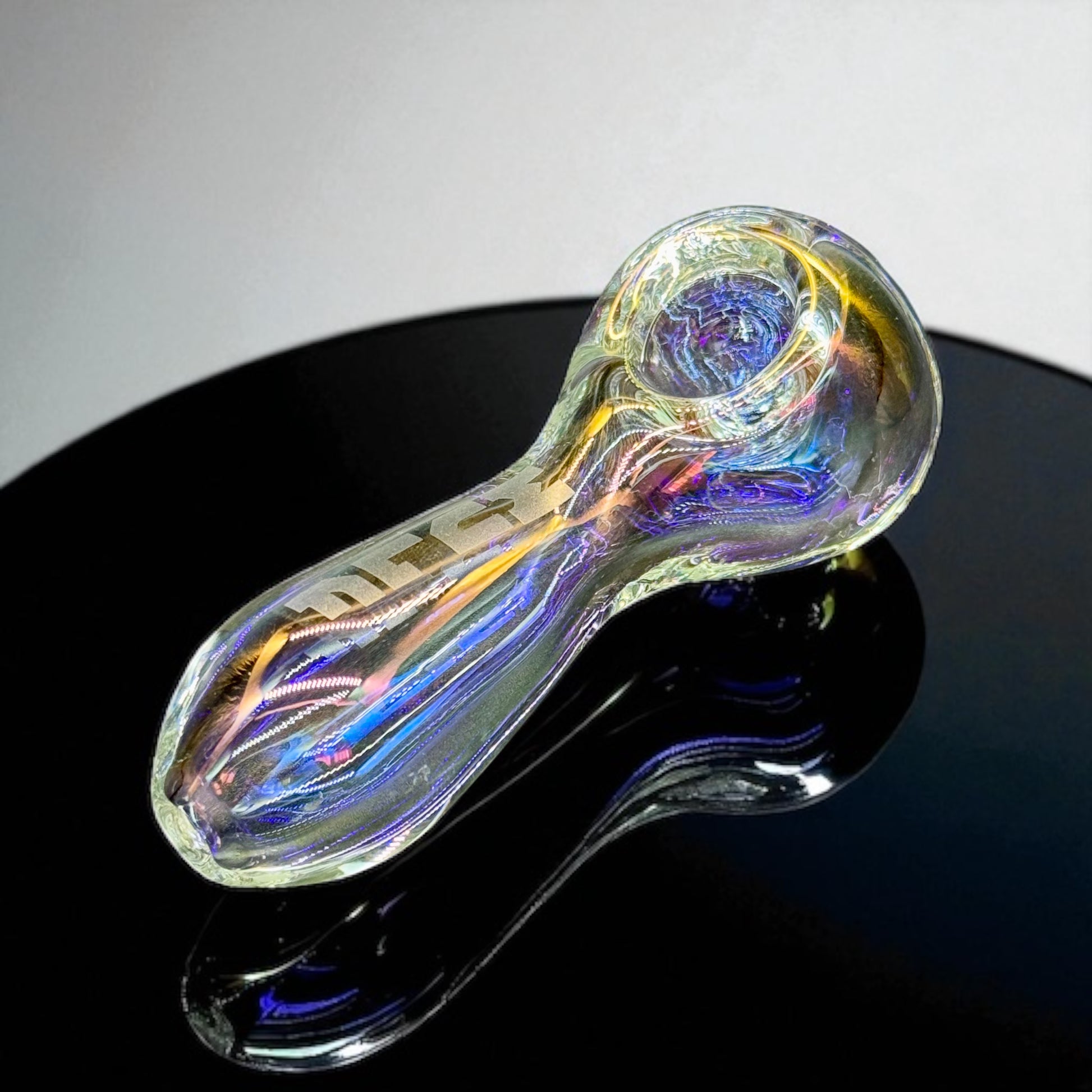 Iridescent glass pipe on a black surface with a white background