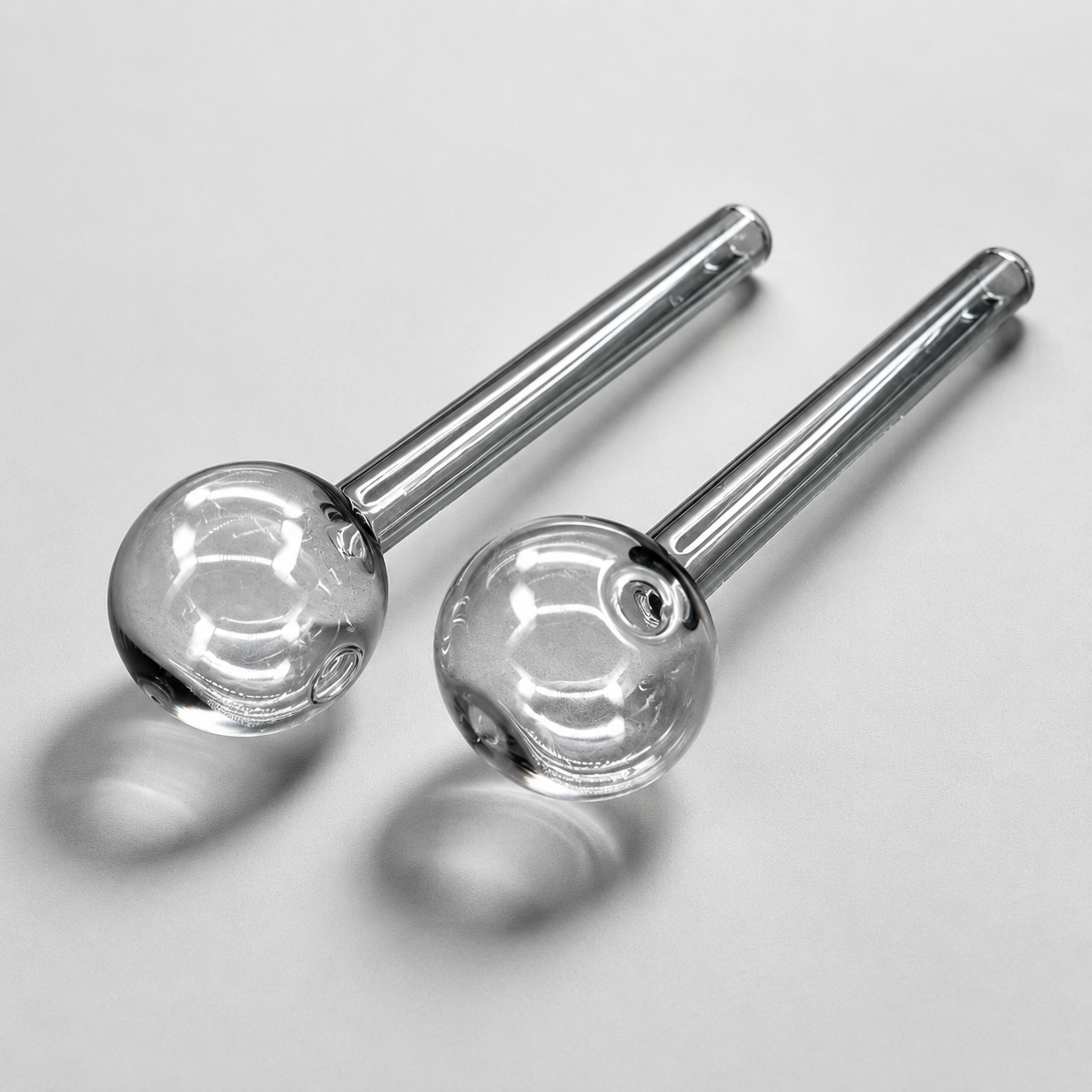 Two glass smoking accessories with metal stems on a light gray background