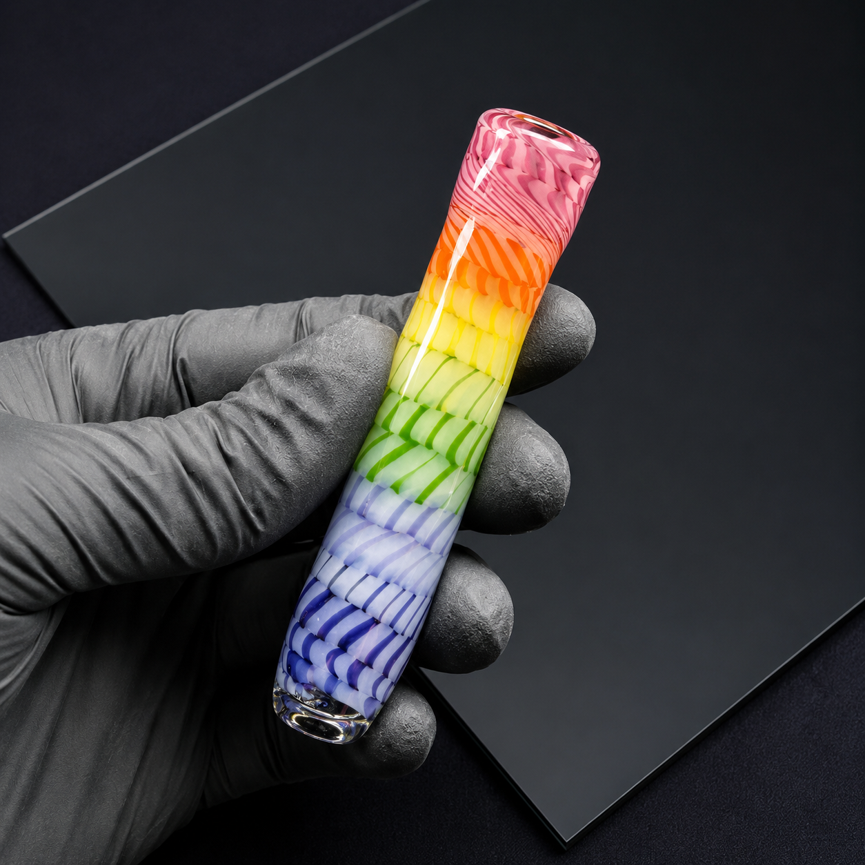 Rainbow-colored glass pipe held by a gloved hand on a black background
