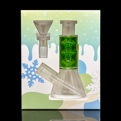 A clear glass water pipe with a bright green geometric patterned neck, shown in front of its printed packaging box. The box features a winter-themed design with snowflakes, a dripping color gradient background, and a white base.