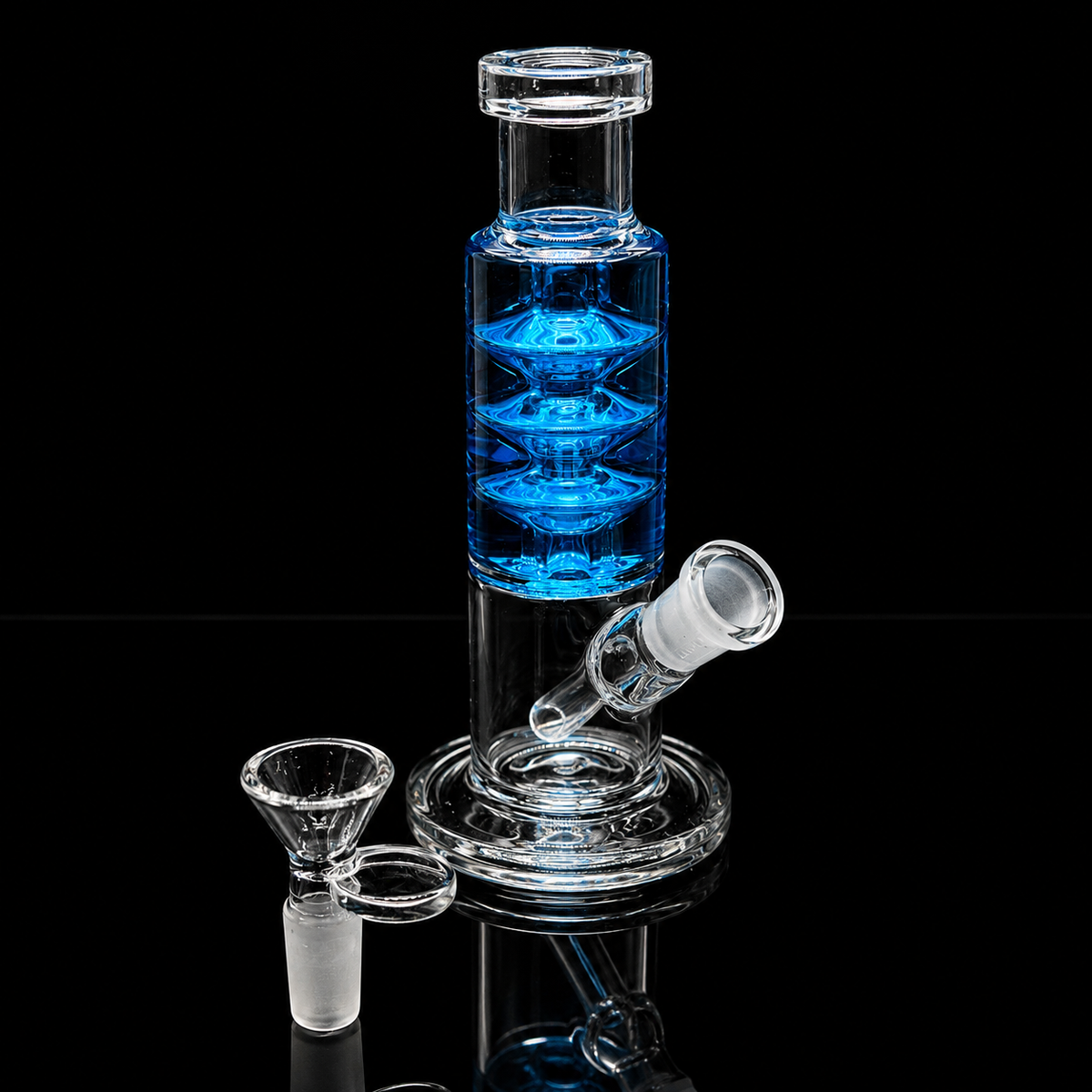 Clear glass water pipe with a blue liquid-filled chamber, shown on a black reflective background with a separate glass bowl piece.