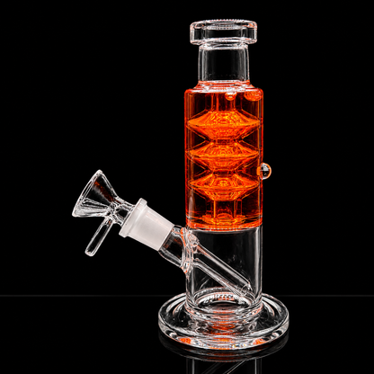 A clear glass water pipe with a cylindrical chamber filled with bright orange liquid, featuring a side neck with a glass bowl and a round base, photographed on a black reflective background.