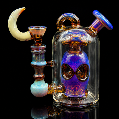 Colorful glass smoking device with alien face design on a black background
