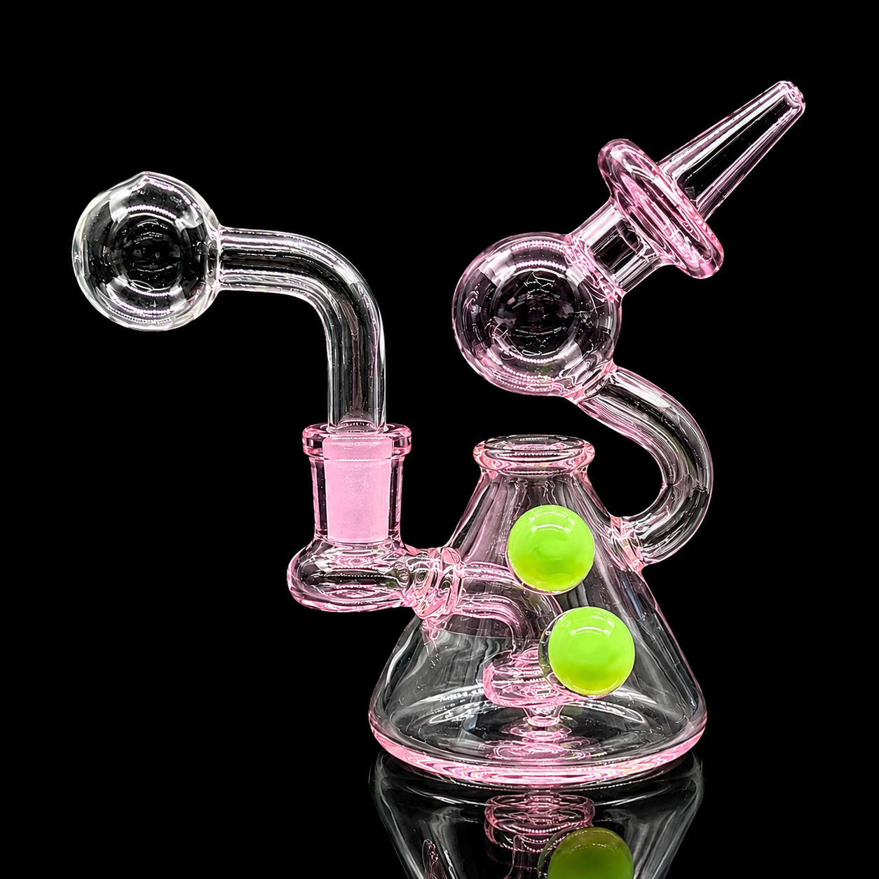 Glass smoking device with pink accents and green balls on a black background