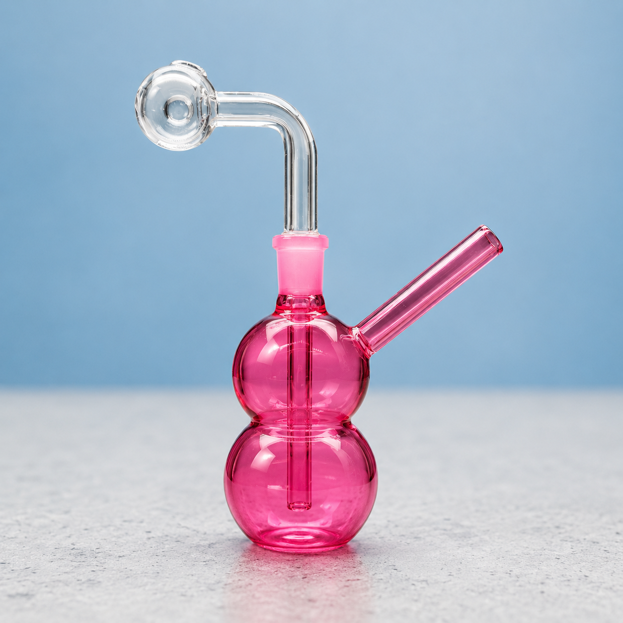 Pink glass smoking device on a light gray surface with a blue background