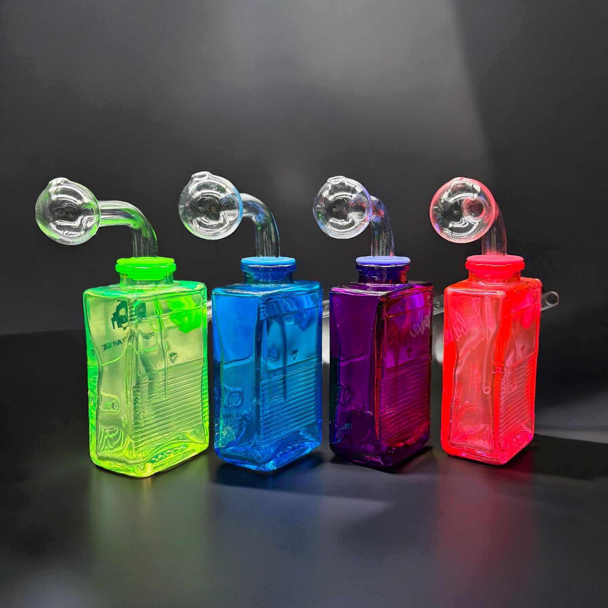 Four colorful Gameboy-style oil burner glass bubblers in green, blue, purple, and hot pink with clear removable parts