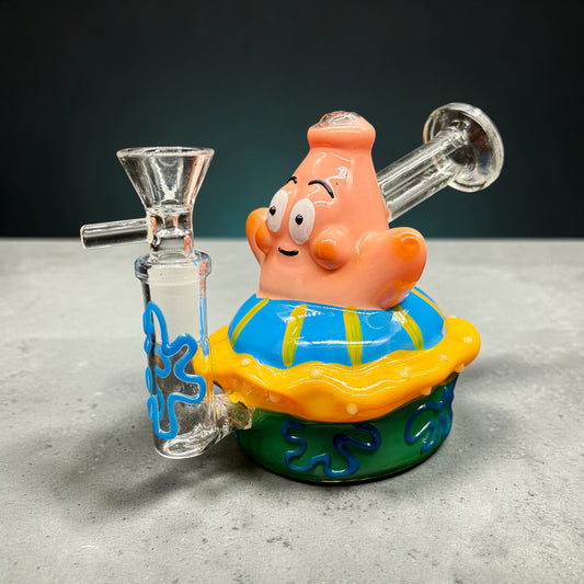 Glass smoking accessory shaped like a cartoon character on a gray surface with a dark background