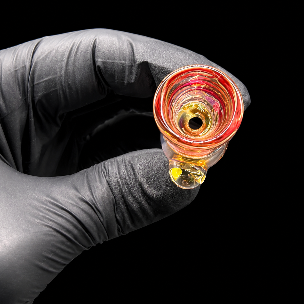 Glass smoking accessory held by a gloved hand against a black background