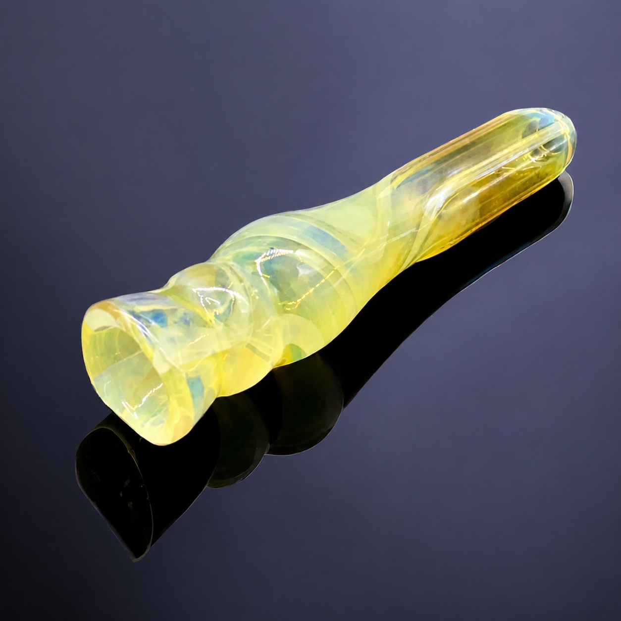 Yellow glass pipe on a reflective black surface with a dark background