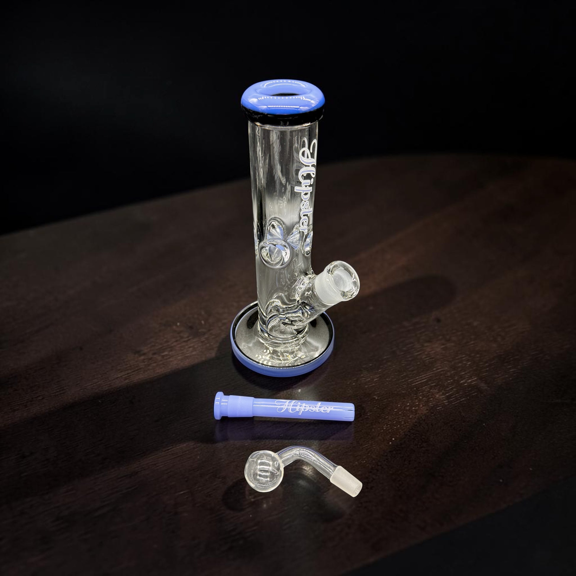Clear glass water pipe with blue accents on a dark wooden surface