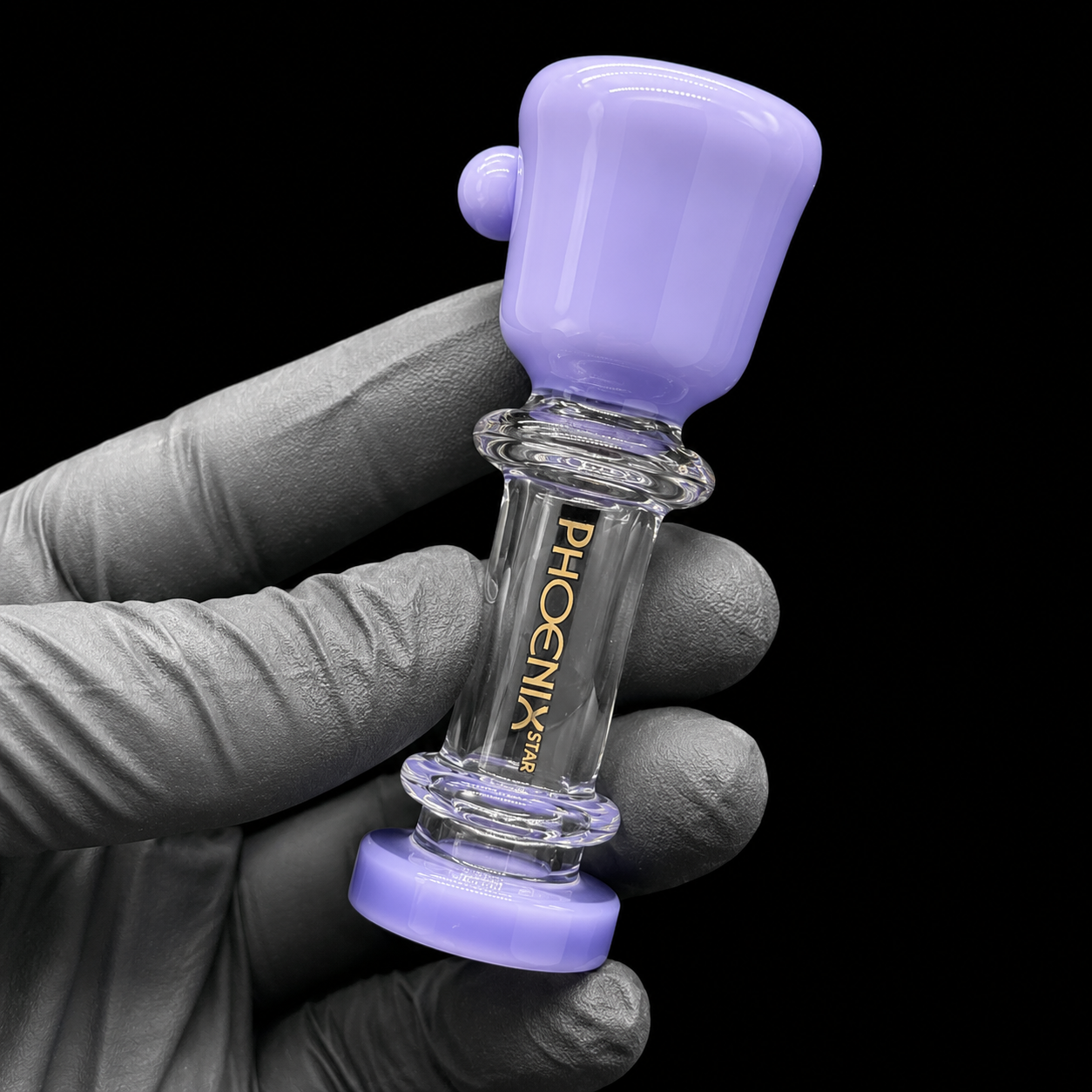 Glass smoking accessory with purple top held by a gloved hand against a black background