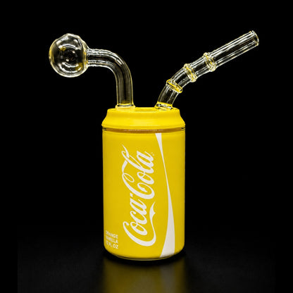 Glass smoking device shaped like a yellow Coca-Cola can on a black background