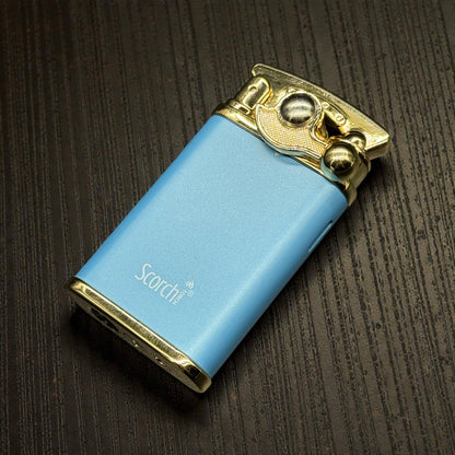 A light blue metallic lighter with gold-toned accents and the brand name 'Scotch' printed on the side, resting on a dark wood-textured background.