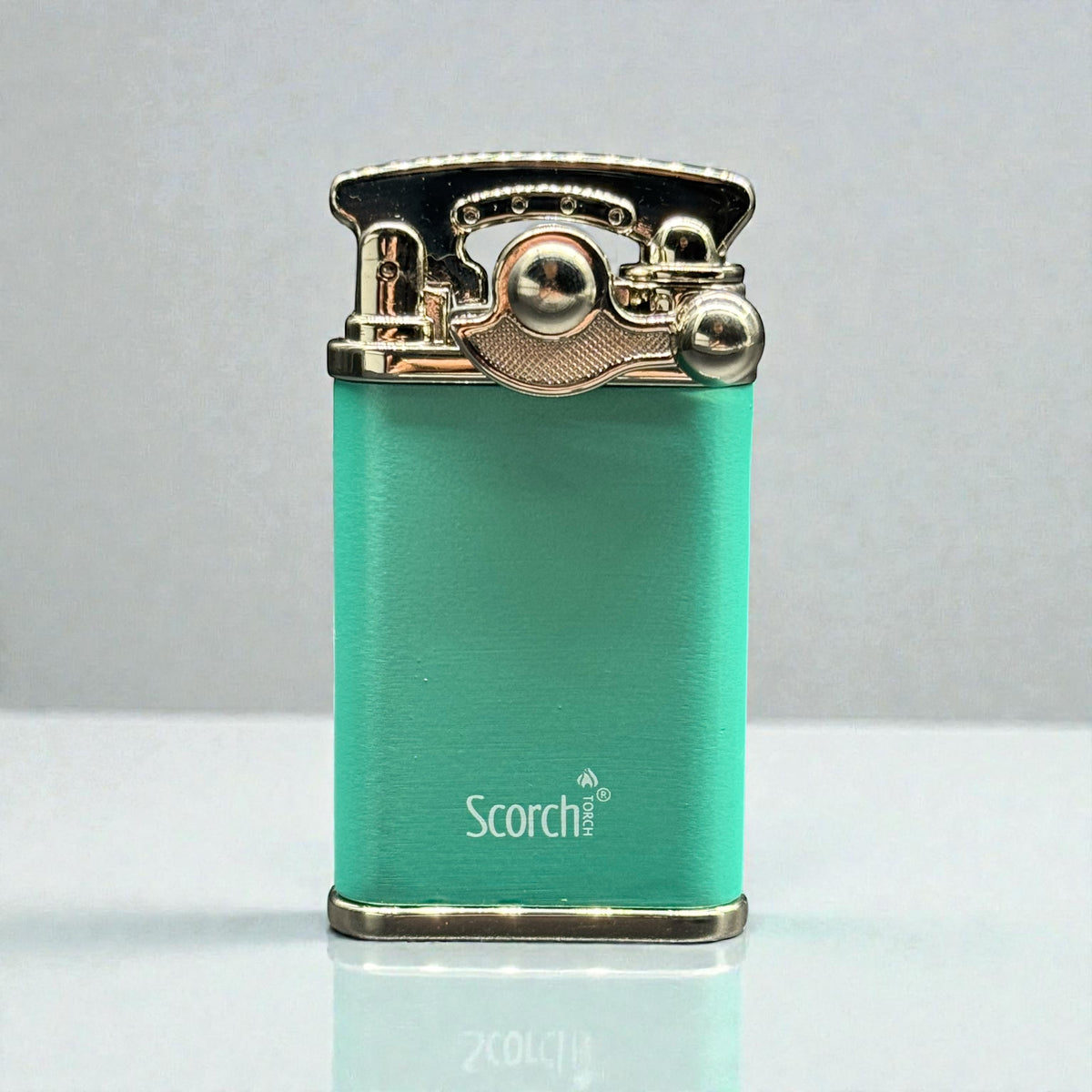A turquoise green portable lighter with polished gold-toned metal accents and the brand name 'Scorch' printed on the front, set against a neutral gray background.