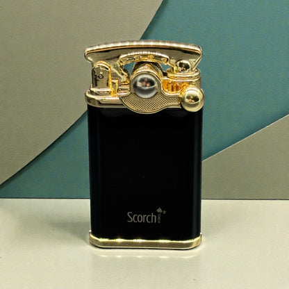 A black Scorch portable lighter with a polished gold-toned metal top and base, standing upright on a light surface against a geometric teal and gray background.
