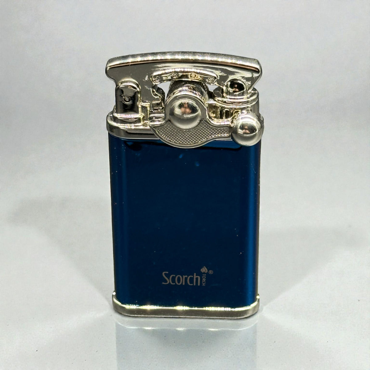 A blue metallic Scorch lighter with a polished silver-toned lighter mechanism on top, standing upright on a light gray reflective surface.