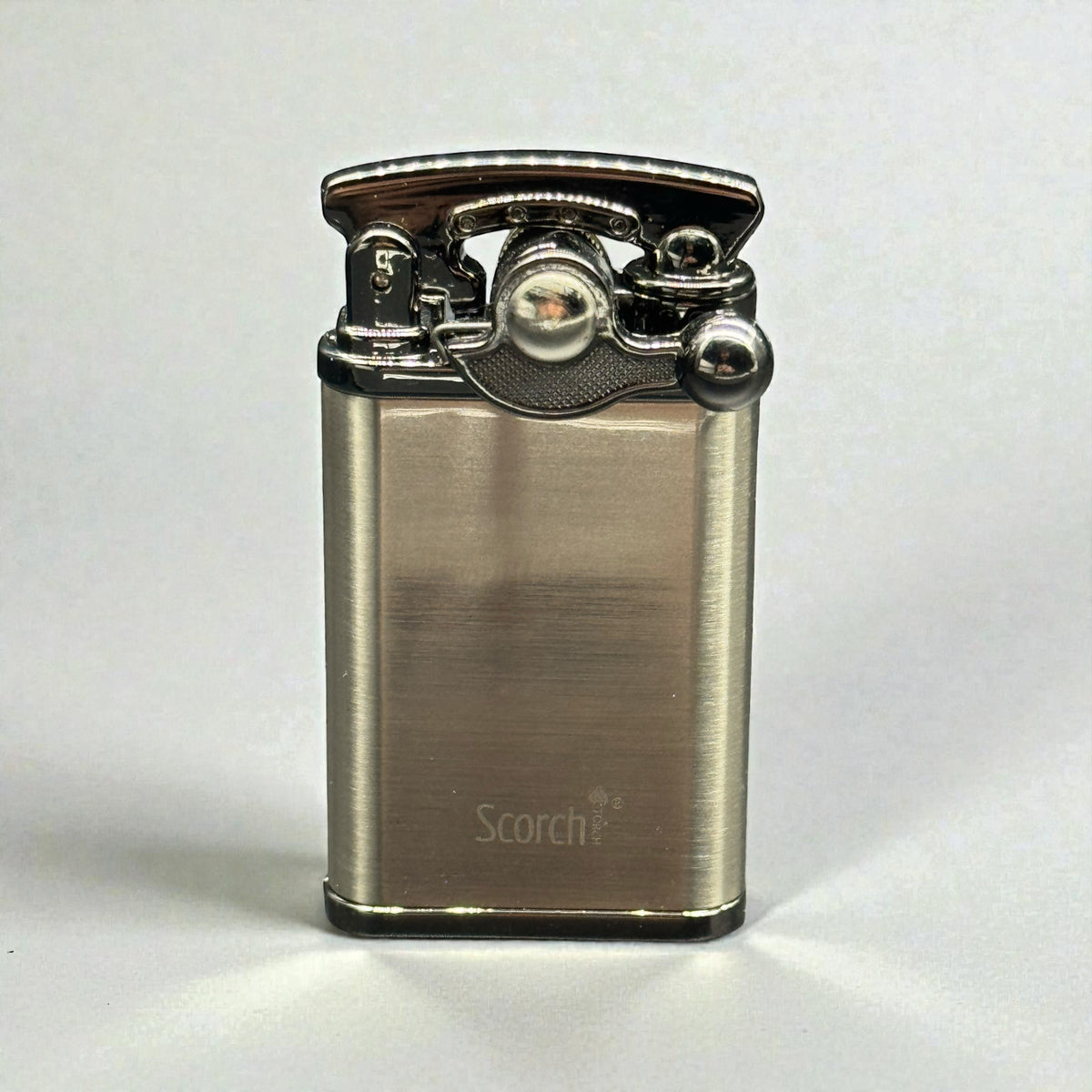 A brushed metal lighter with a polished chrome top mechanism, featuring the 'Scorch+' brand name printed near the bottom, set against a plain light gray background.