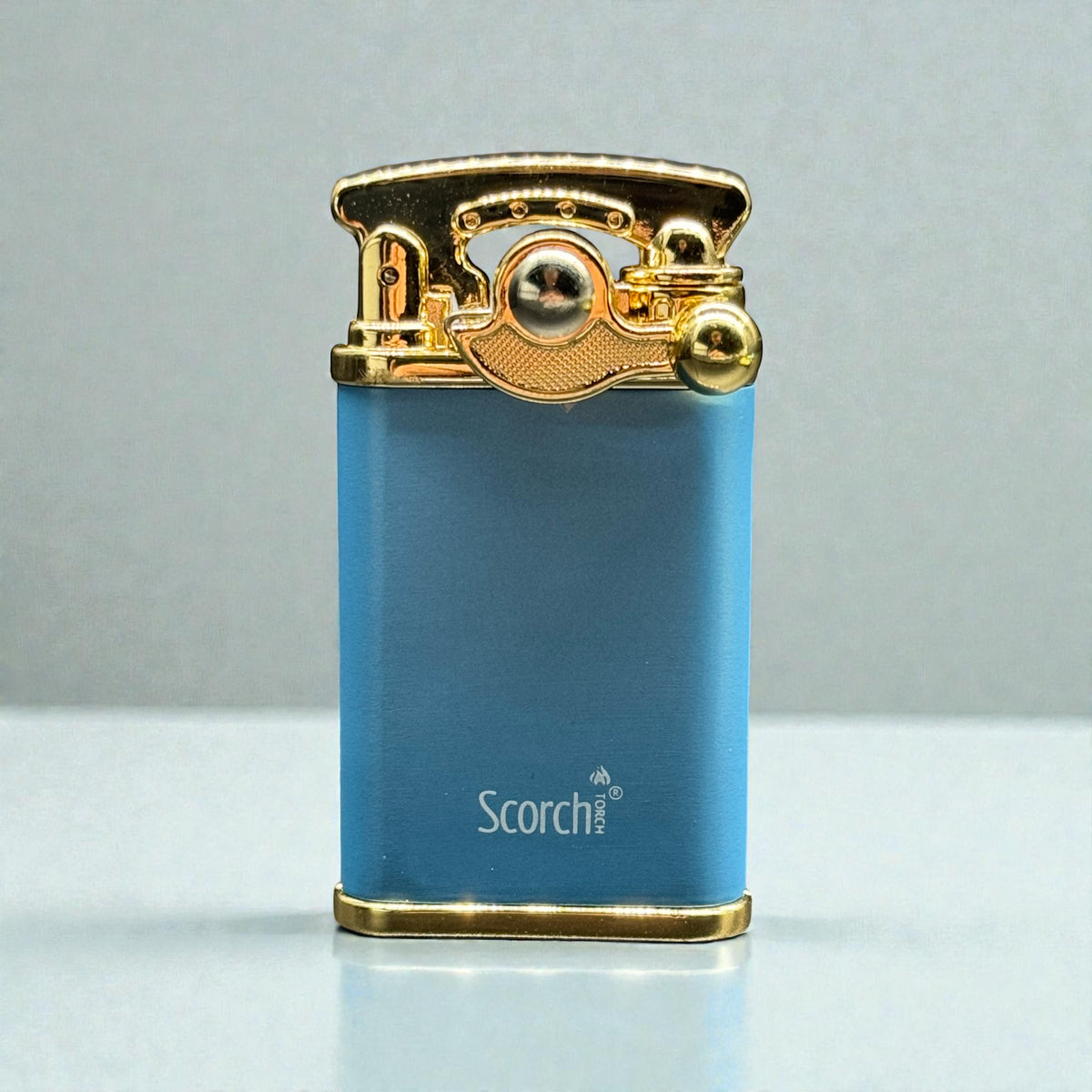 A blue metallic lighter with a gold-toned top mechanism and base, featuring the 'Scorch' brand name printed in white on the front, set against a neutral gray background.