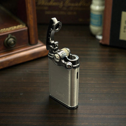 A brushed silver metal lighter with a black flip-up flame guard, standing open on a dark wooden tabletop with a blurred background.