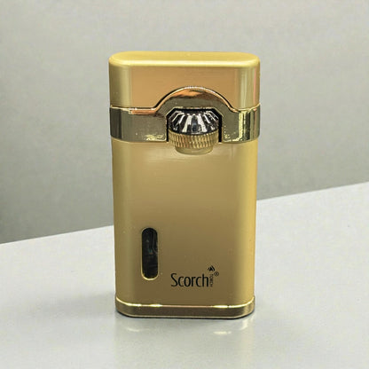 A gold metallic Scorch brand lighter with a polished chrome ignition button, standing upright on a light gray surface.