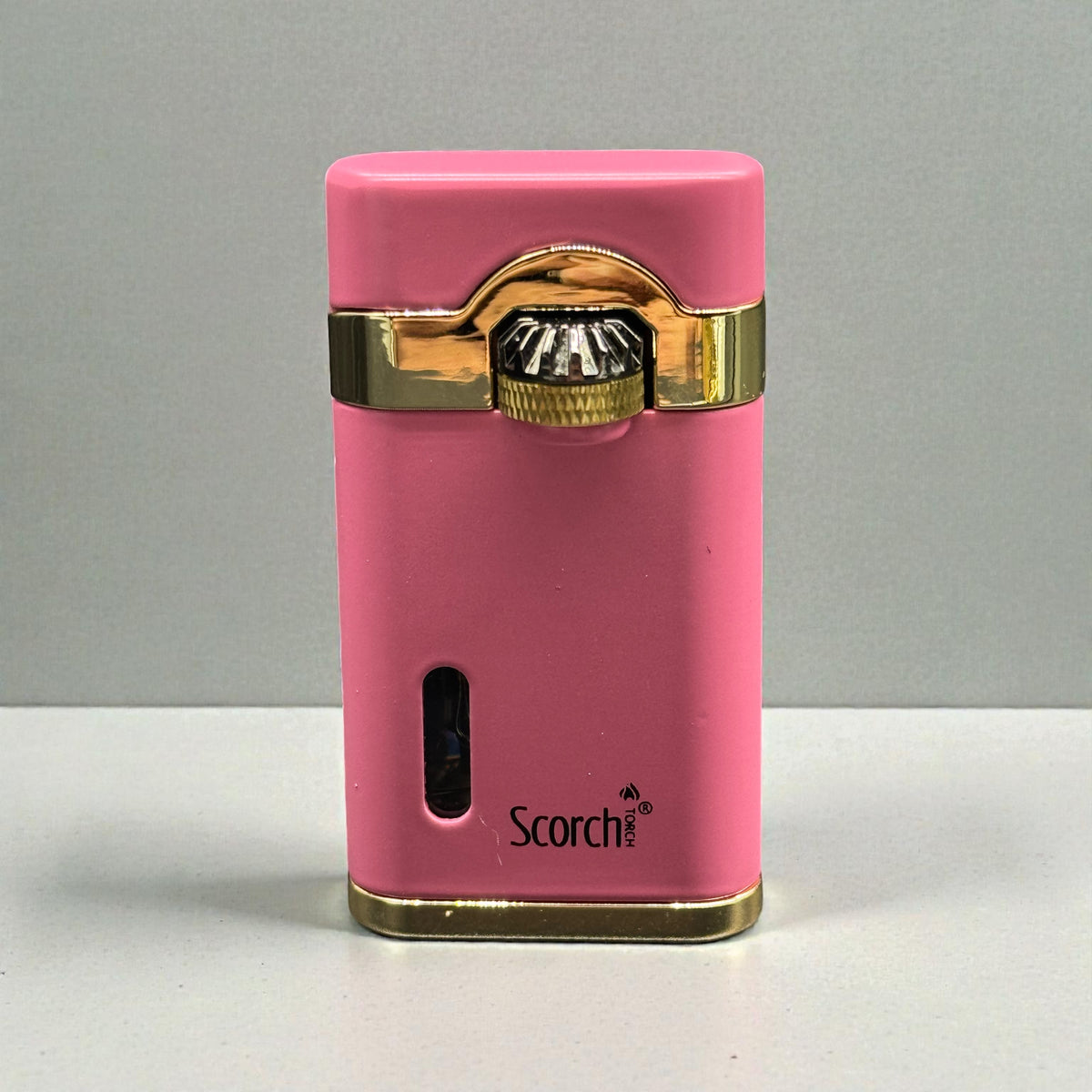 A pink Scorch electronic cigarette lighter with gold trim and a metallic ignition button, standing upright on a light gray surface against a gray background.