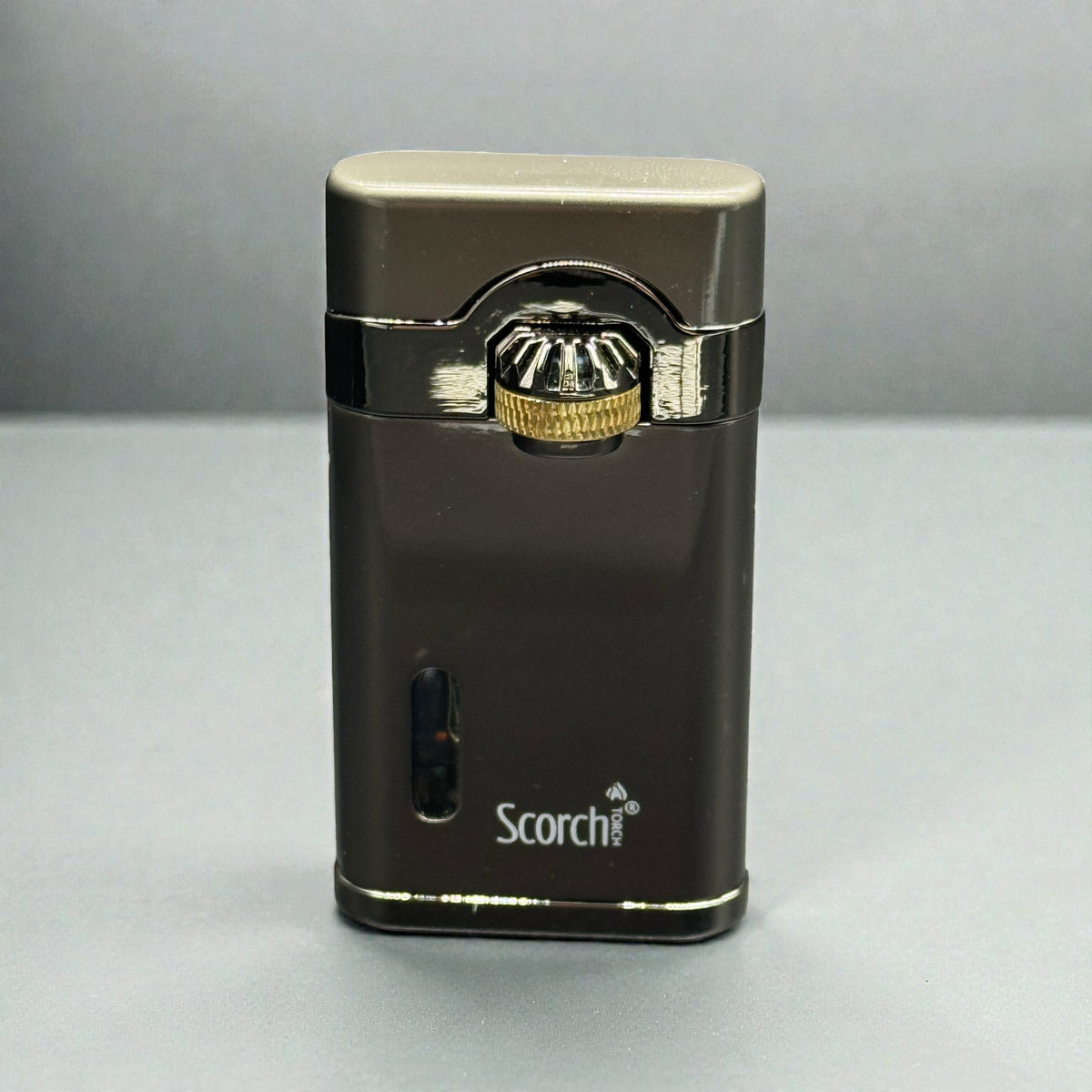 A metallic dark brown and silver Scorch portable lighter with a gold accent on the ignition button, standing upright on a gray surface.
