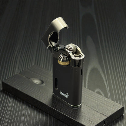 A black metallic pocket lighter with a silver flip-up lid and gold-toned ignition detail, standing on a dark wooden display block against a dark wood-grain background. The brand name 'Scotch' is printed on the lower front.