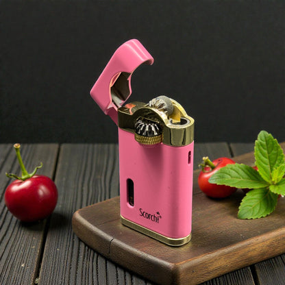 A pink Scorch portable electric lighter with gold-tone metal accents, shown open on a wooden board with red cherries and mint leaves on a dark rustic table.