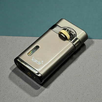 A metallic silver Scotch lighter with a gold-toned ignition dial, resting on a speckled gray surface against a teal background.
