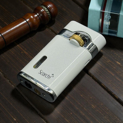 A white and silver Scorch electronic lighter with a gold-toned dial, resting on a dark wooden surface next to a wooden mallet and a light blue box.