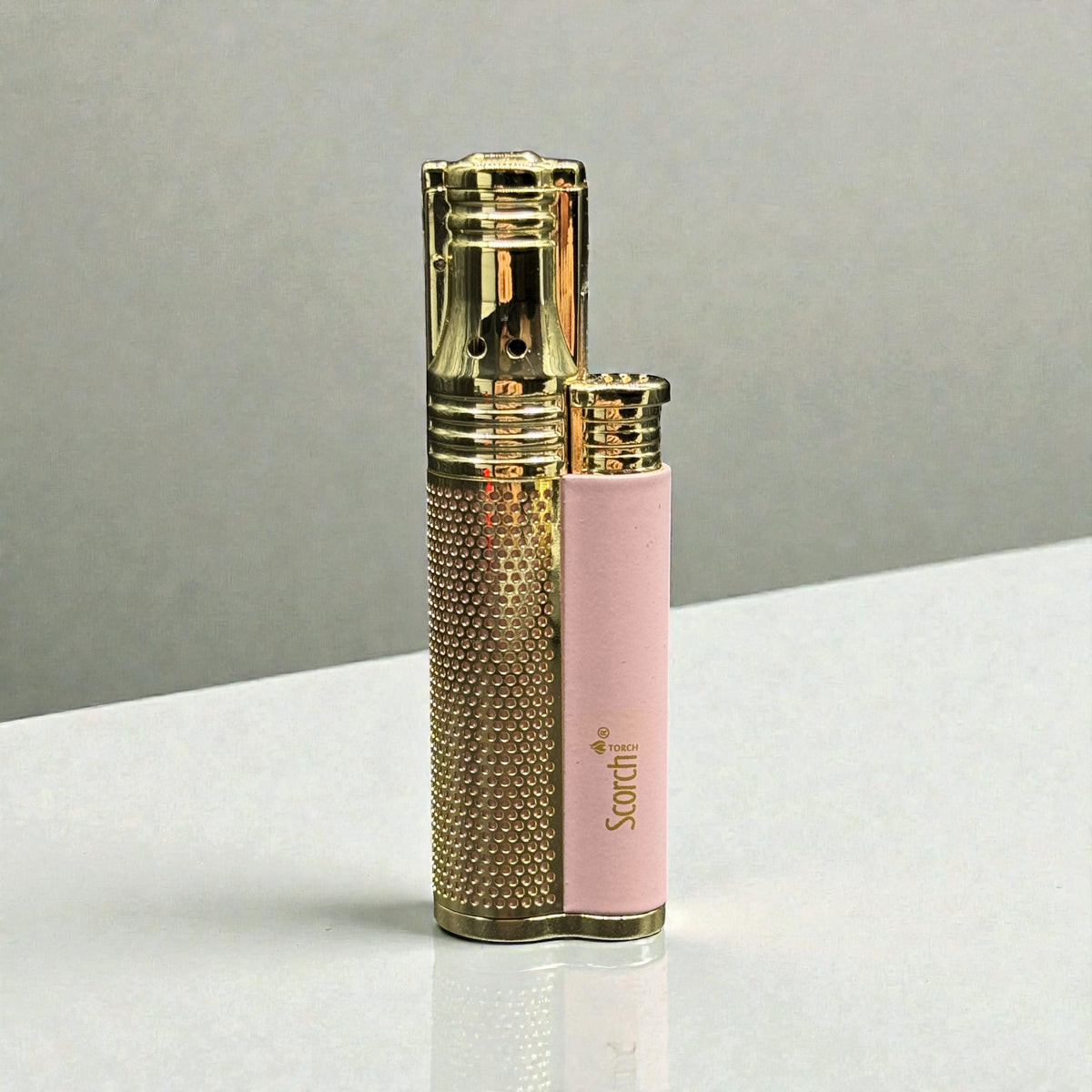 A gold-plated lighter with a textured grip and a pink protective sleeve printed with the brand name 'Sardi', set on a white surface against a gray background.