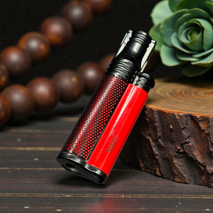 A red and black textured lighter with the brand name 'Socra' printed on the side, resting on a rustic wooden block with a dark wood background and blurred decorative beads and a succulent.