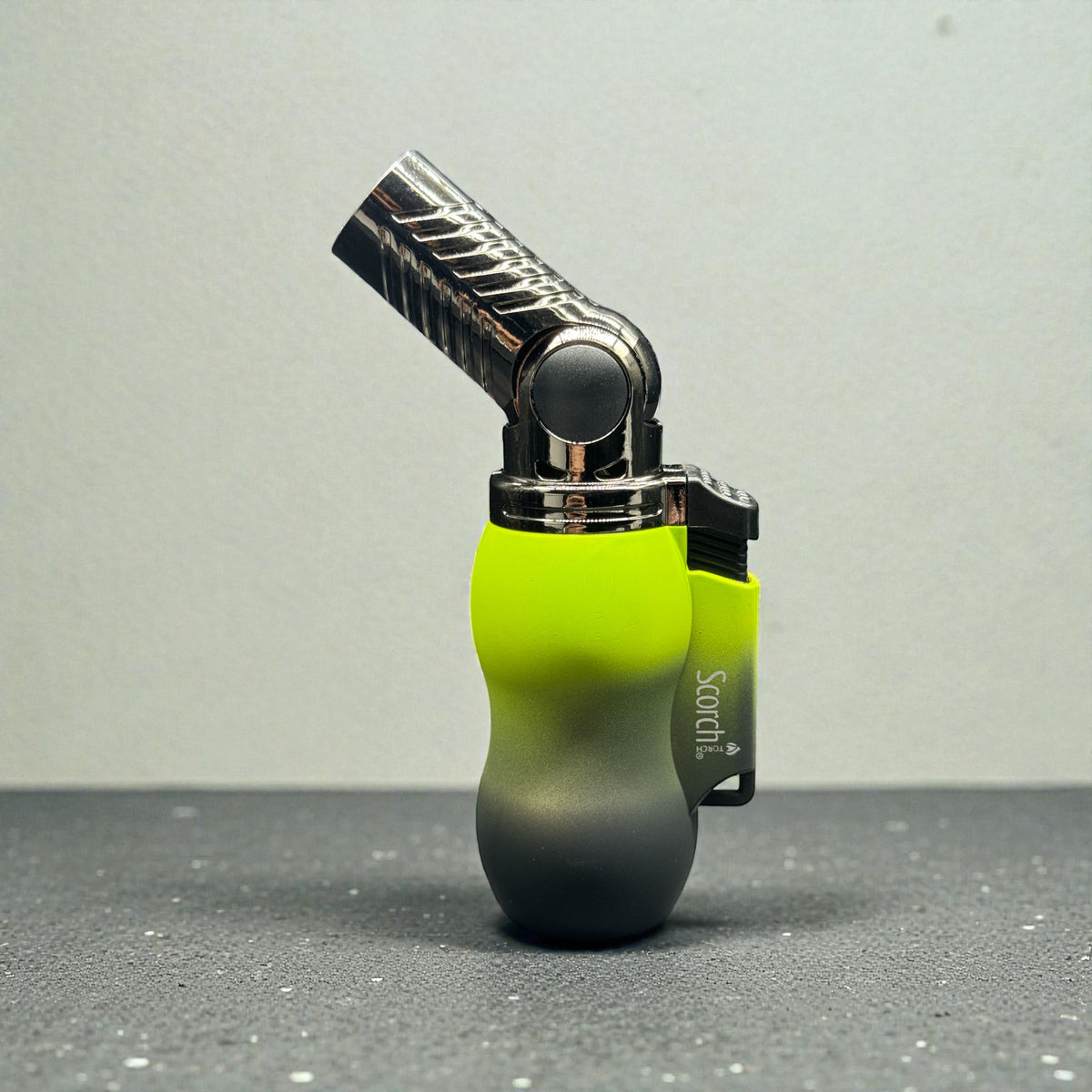A SOROTUL torch lighter with a bright neon yellow-green to dark gray gradient body, standing upright on a dark gray textured surface against a light gray background.