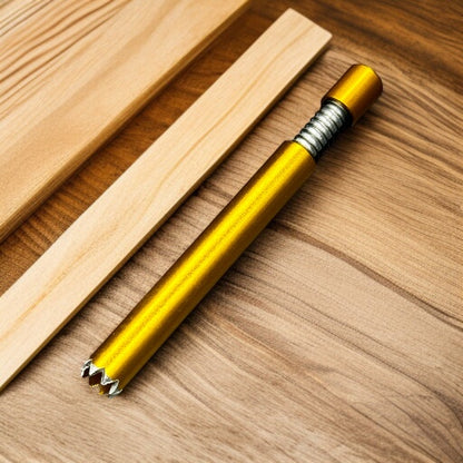 A metallic gold and silver wood drill bit with a threaded handle, resting diagonally on a wooden surface next to two light wood strips.