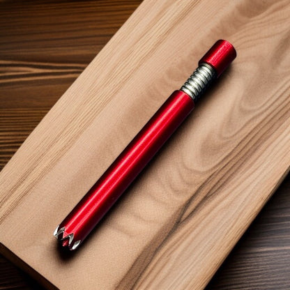 A red metallic pencil with a textured silver grip and a pointed silver tip, resting diagonally on a light wood grain board over a dark wood surface.