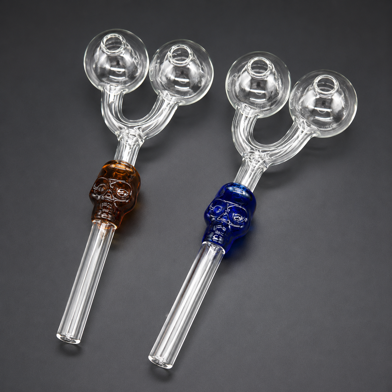 Two glass smoking accessories with skull designs on a dark gray background