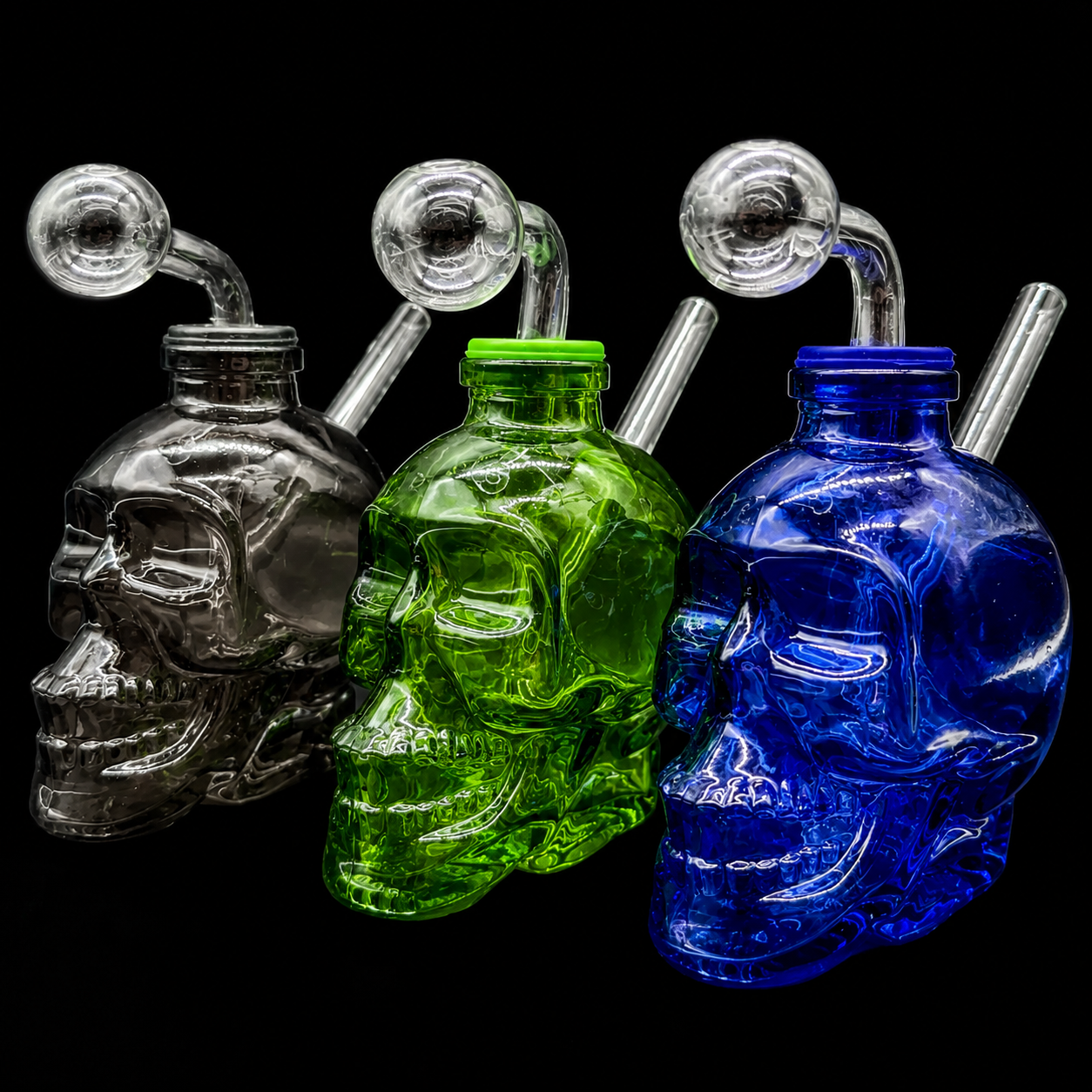 Three glass skull-shaped pipes in silver, green, and blue on a black background.