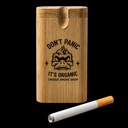 A rectangular wooden cigarette case with a lid, engraved with the text 'DON'T PANIC IT'S ORGANIC UNIQUE SMOKE SHOP' and a cartoon face, shown on a black background with a single cigarette in front.
