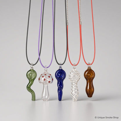 Assorted mini hand-blown glass pipe necklaces in different colors and designs including green wavy, mushroom, blue spiral, clear swirl, and amber styles hanging on cords