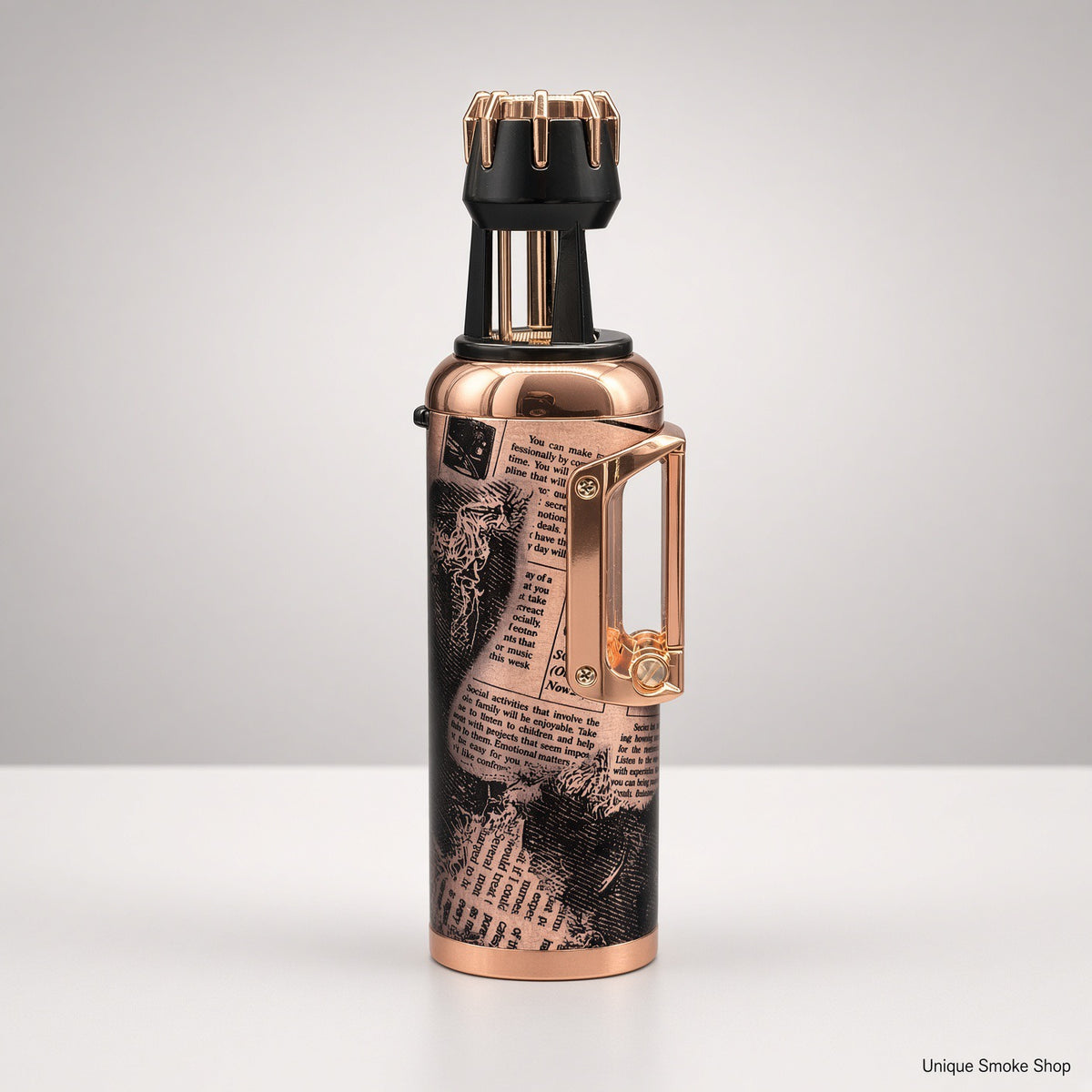A metallic copper vape device with a black and white newspaper print graphic on the body, a black mouthpiece with gold accents, and a gold side clip, shown on a light gray background.