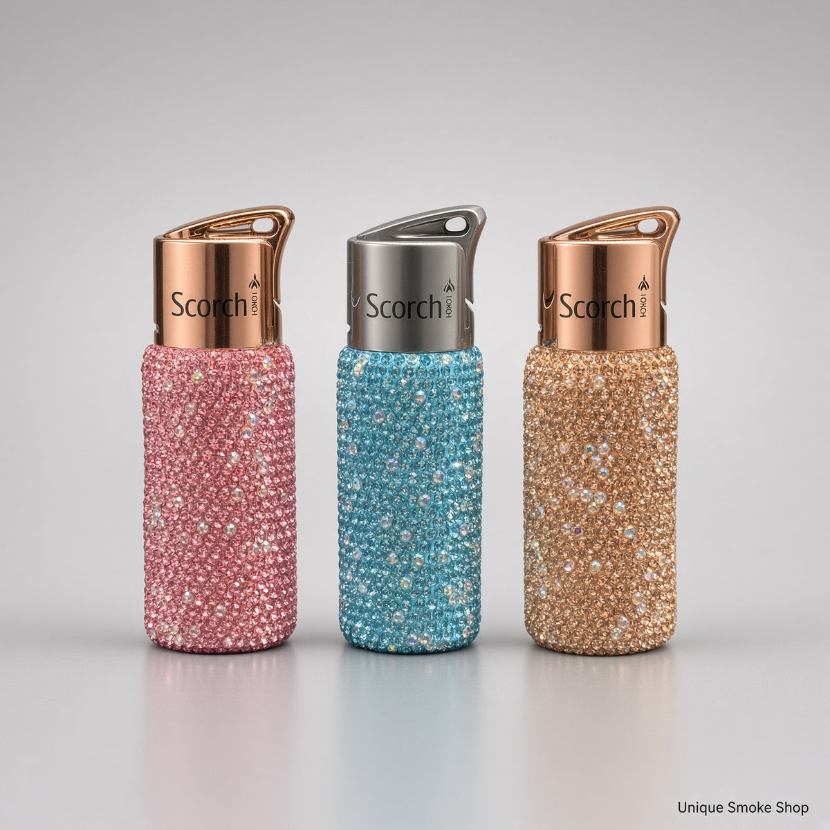 Scorch 61892 rhinestone single flame torch lighters in pink, teal, and champagne on a light gray studio background